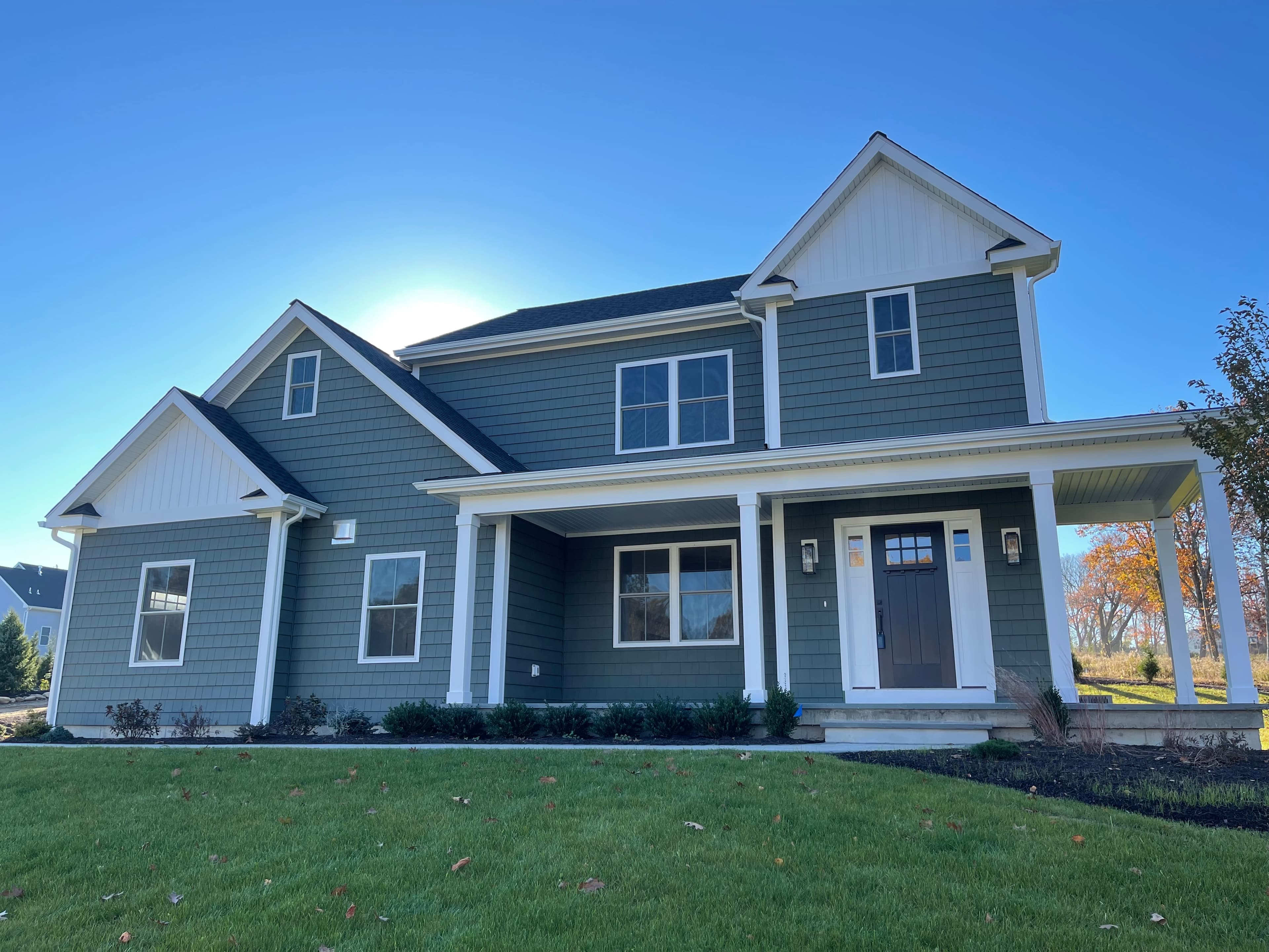 Horizontal lap siding in a dark green-gray, with white corner boards and window trim.