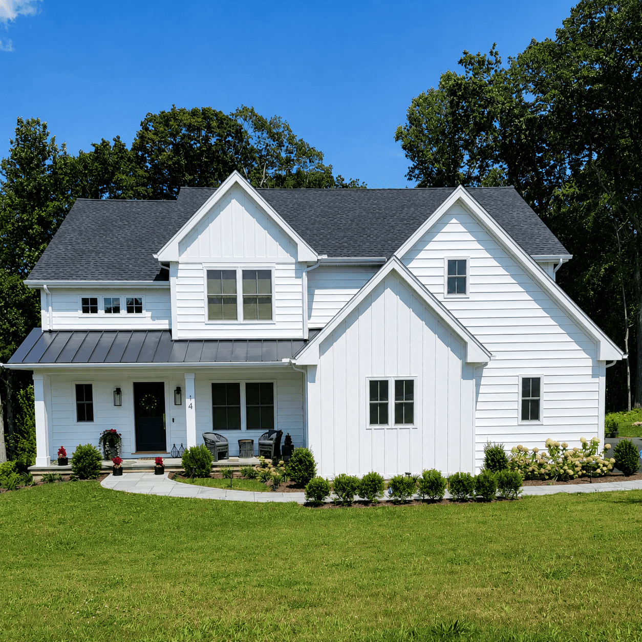 White board-and-batten farmhouse with steep gables, a dark shingle roof and a landscaped walkway to the front entry.