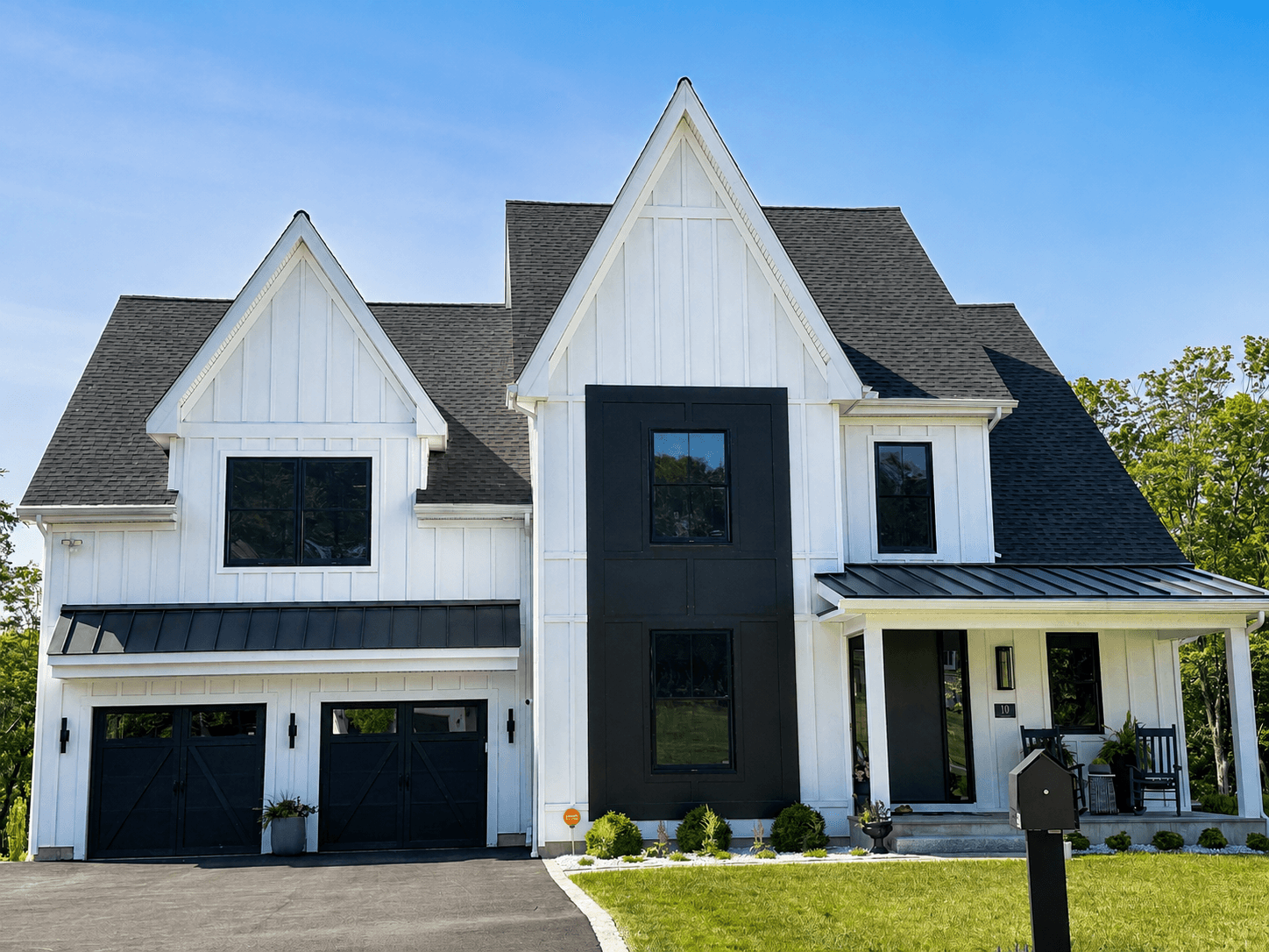 White board-and-batten exterior with a contrasting black vertical siding panel, black windows, a black metal porch roof and a two-car garage.