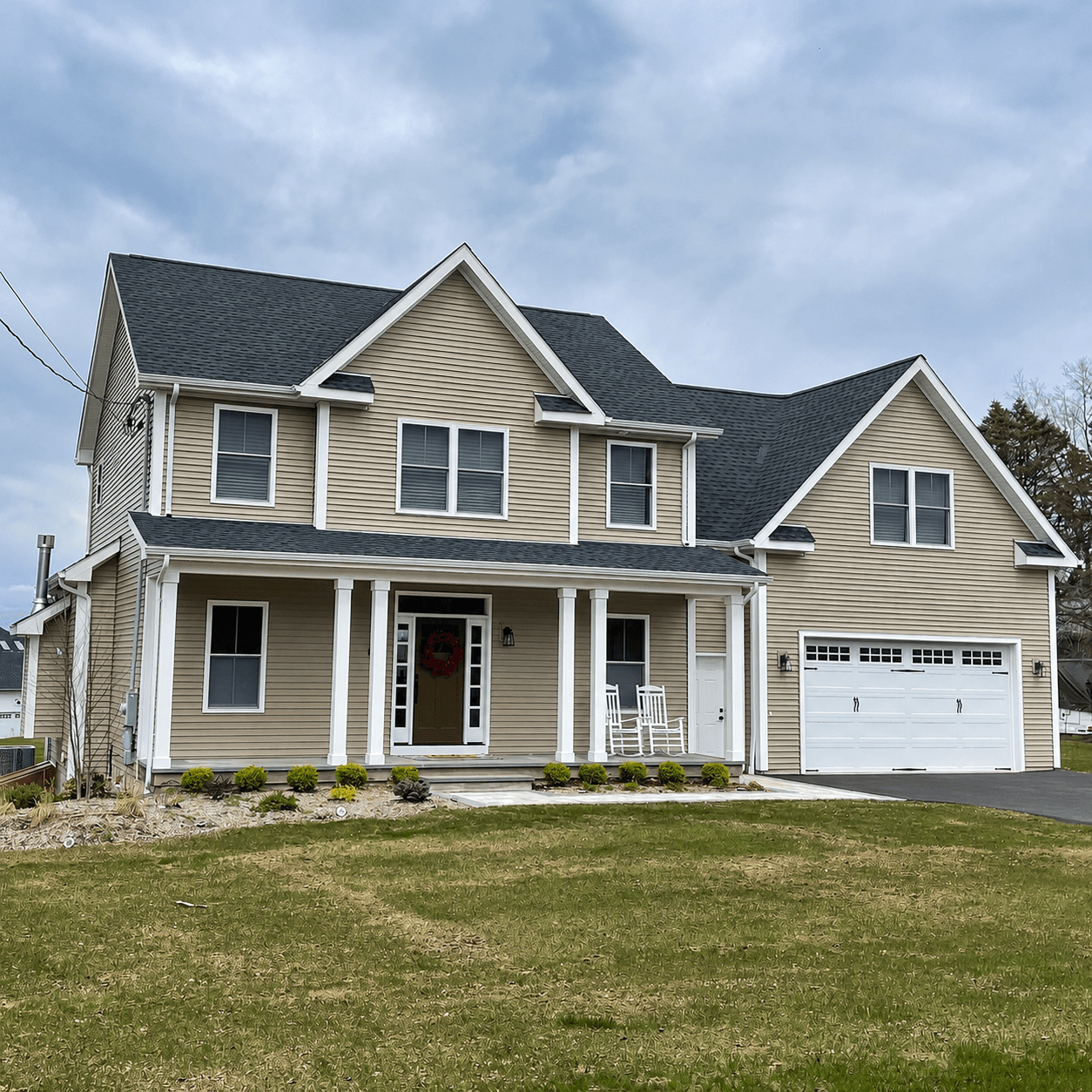 Tan horizontal siding on a two-story home with crisp white corner boards, window trim and porch columns, beside an attached garage.