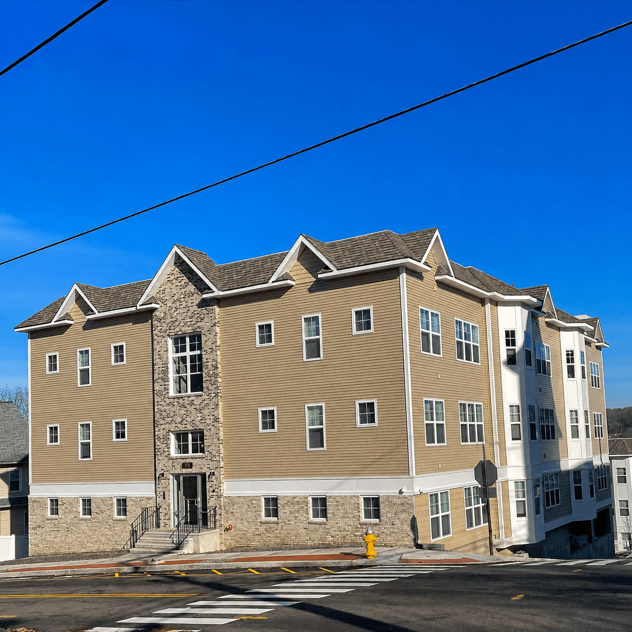 Three-story multifamily building clad in clay-toned horizontal siding with a stone-veneer base and white trim, on a street corner.