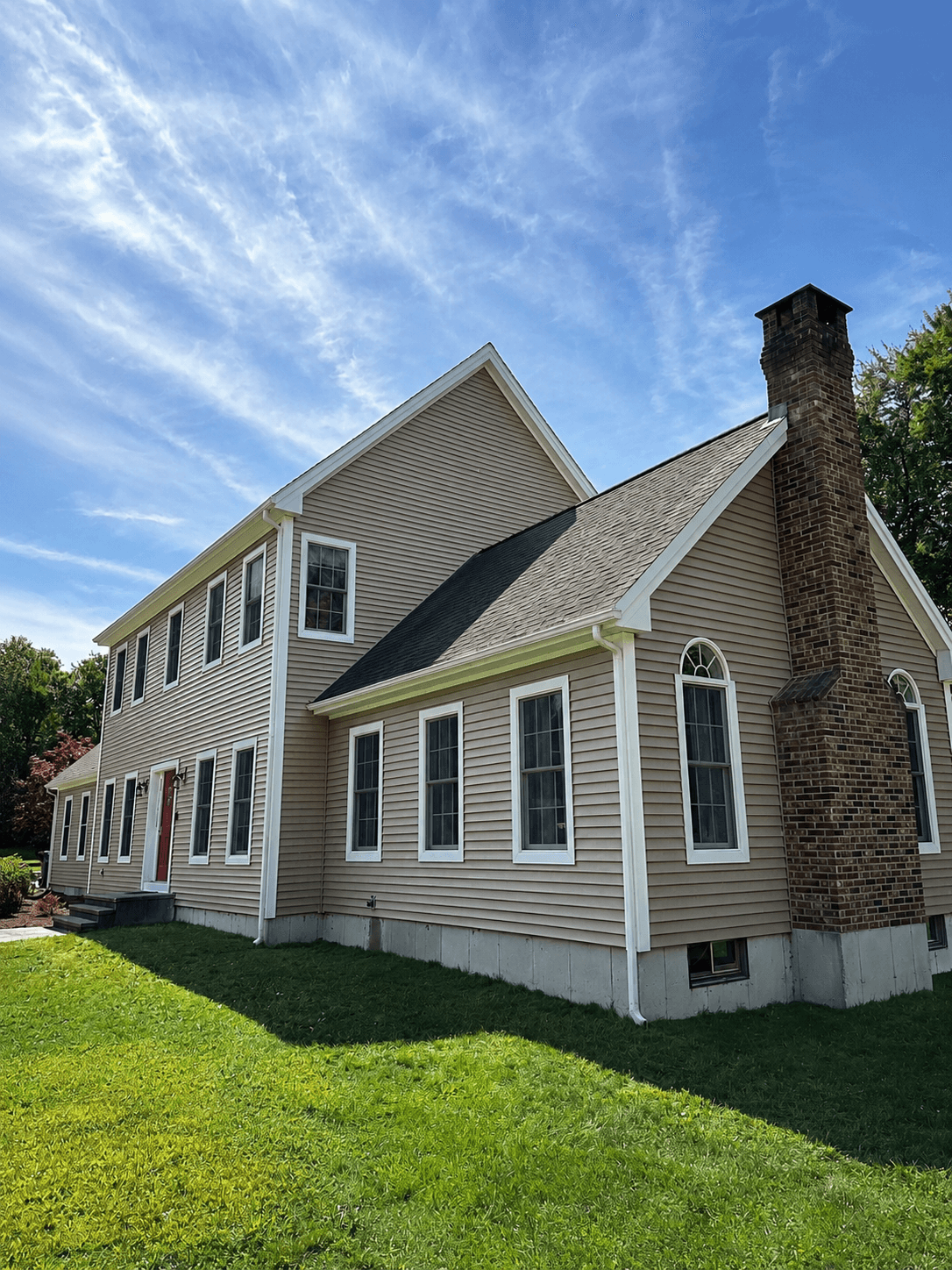 Side elevation of a beige horizontal-siding home showing the eave line, white soffit and fascia, gable rake trim and a brick chimney.