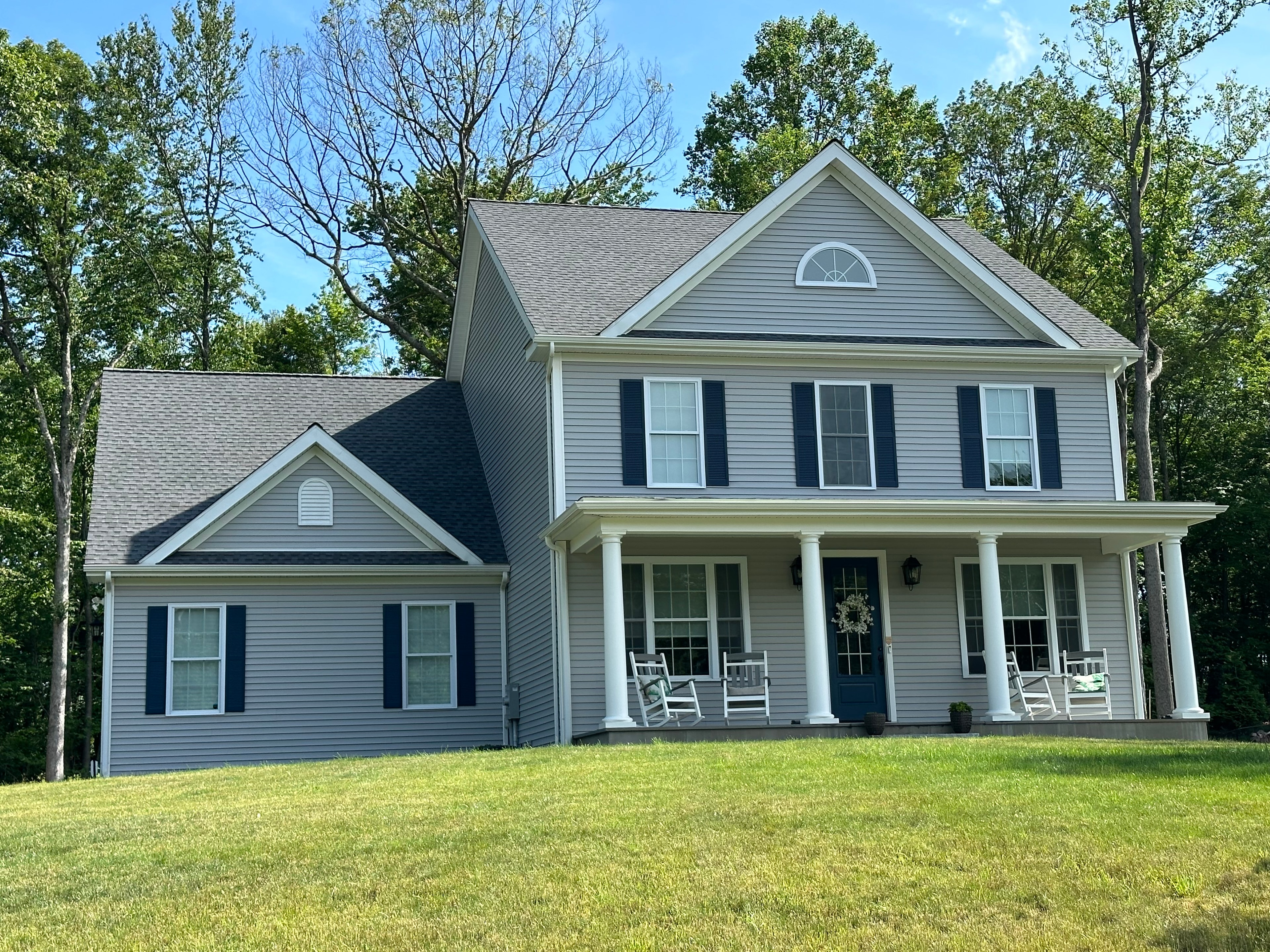 Light gray horizontal siding with black shutters, white trim, a columned covered porch and a half-round gable vent.